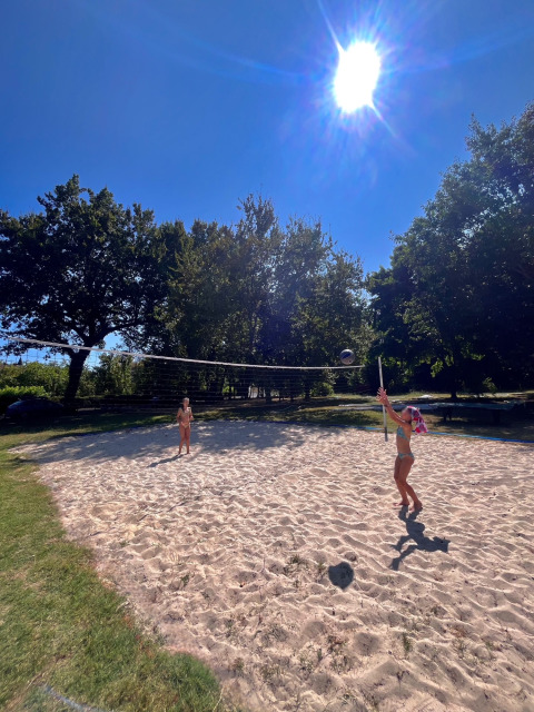 Due persone giocano a beach volley sotto il sole al Camping Le Périgord in Nouvelle-Aquitaine, Francia.