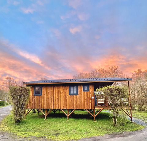 Baita in legno su palafitte al Camping Le Périgord in Nouvelle-Aquitaine, Francia, con cielo al tramonto colorato.