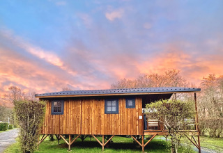 Baita in legno su palafitte al Camping Le Périgord in Nouvelle-Aquitaine, Francia, con cielo al tramonto colorato.
