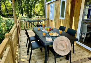 Terrasse mit Holztisch, sechs Stühlen, Saft, Obst, Melonen und Strohhut bei Camping Le Périgord in Nouvelle-Aquitaine.