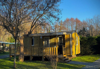 Casetta in legno a Camping Le Périgord, Nouvelle-Aquitaine, Francia, circondata da prato verde e alberi in una giornata soleggiata.