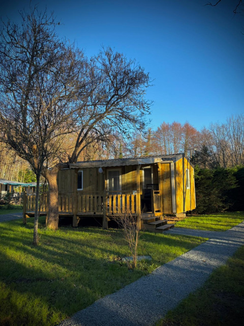 Cabaña de madera en Camping Le Périgord, Nouvelle-Aquitaine, Francia, rodeada de césped verde y árboles al sol.