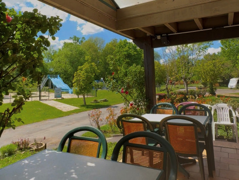 Udsigt fra terrassen ved Camping Le Périgord med borde, stole og legeplads i baggrunden, Frankrig.