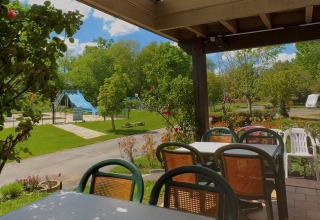 Blick von der Terrasse im Camping Le Périgord mit Tischen, Stühlen und Spielplatz im Hintergrund, Frankreich.