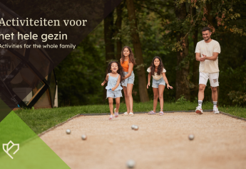 Family enjoys playing an outdoor game together on a sunny day near a lodge, surrounded by green nature.