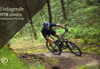 Mountainbiker rijdt een uitdagend bospad tijdens een MTB-clinic bij een lodge, omgeven door natuur.