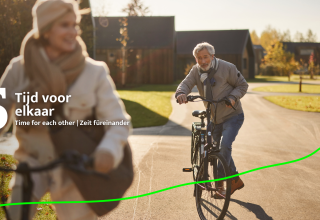 Een ouder koppel fietst samen langs een zonnig pad bij Unbrick One | Sauna glamping tussen de huisjes.