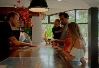 Gezin checkt in aan de receptie van een glampingverblijf, gesprek met receptionist aan de balie.