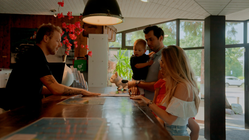 Gezin bij de receptie van een glamping-accommodatie, in gesprek met de receptionist aan de balie.