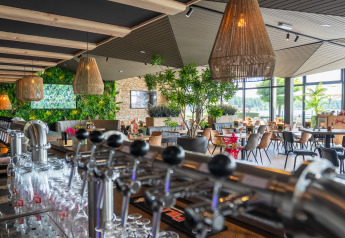 Zona bar e ristorante moderna con piante e ampie finestre in una sistemazione glamping.