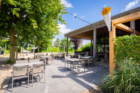 Outdoor terrace with tables and chairs at a glamping accommodation, surrounded by trees and plants.