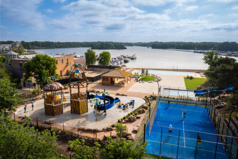 Modern glamping site featuring a playground, padel court, pool and scenic lake views with boats.