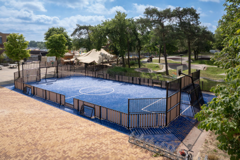 Campo multisport blu in una struttura glamping, circondato da alberi, rastrelliere bici e aree relax.