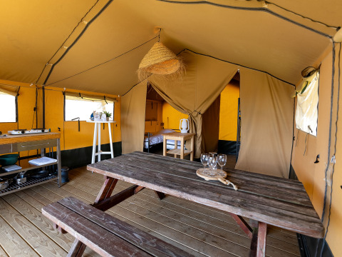 Interior de una tienda safari en Marina Heeg, Países Bajos, con mesa, cocina y área de dormitorio.