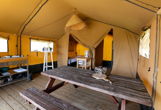 Innenraum eines Safarizeltes mit Holztisch, Küche und Schlafzimmer in Marina Heeg, Niederlande.