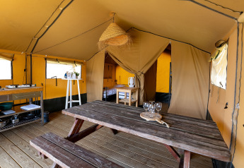 Interior de una tienda safari en Marina Heeg, Países Bajos, con mesa, cocina y área de dormitorio.