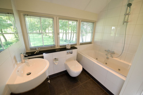 Baño moderno con bañera, ventanales y luz natural en Wellness Lodge XL, Hof van Salland, Países Bajos.