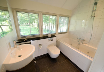 Bagno moderno con vasca, finestre grandi e luce naturale in Wellness Lodge XL, Hof van Salland, Paesi Bassi.