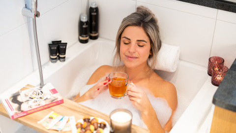 Mujer relajándose en una bañera con burbujas, té, snacks y libros en Wellness Lodge XL, Hof van Salland, Países Bajos.