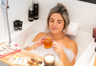 Mujer relajándose en una bañera con burbujas, té, snacks y libros en Wellness Lodge XL, Hof van Salland, Países Bajos.