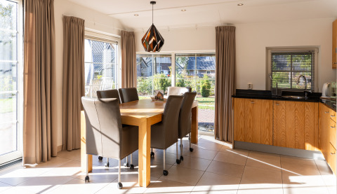 Spiseområde med store vinduer, beige gardiner og træmøbler i Wellness Lodge XL, Hof van Salland, Holland.