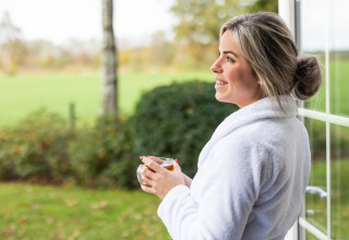 Woman in a white bathrobe enjoying tea by the door of Wellness Lodge XL at Hof van Salland, Netherlands.