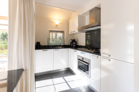Modern kitchen with white cabinets, gas stove, and oven in Wellness Lodge XL, Hof van Salland, Netherlands.