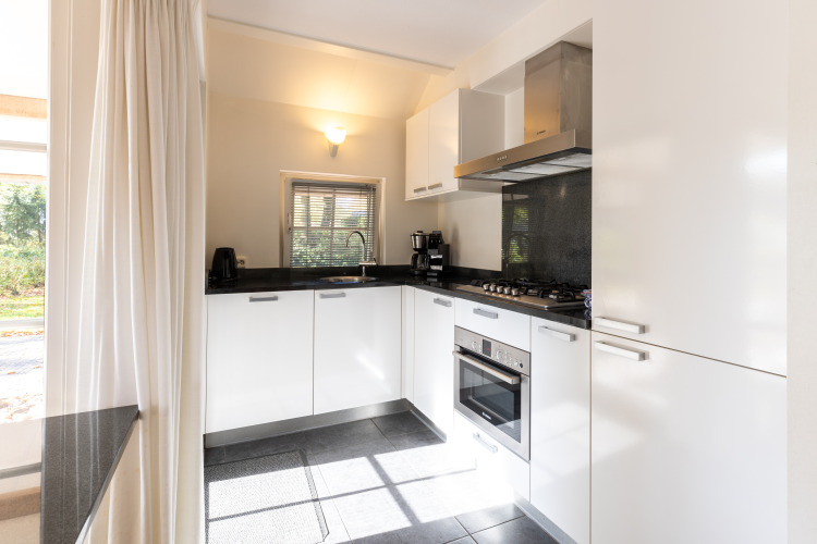 Cocina moderna con gabinetes blancos, estufa de gas y horno en Wellness Lodge XL, Hof van Salland, Países Bajos.