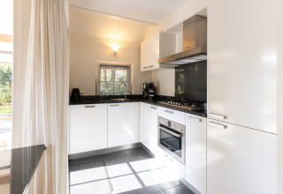 Modern kitchen with white cabinets, gas stove, and oven in Wellness Lodge XL, Hof van Salland, Netherlands.