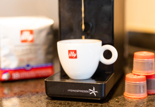 En illy kaffemaskine og kop på Wellness Lodge XL, Hof van Salland, med kaffekapsler og kaffe i baggrunden.