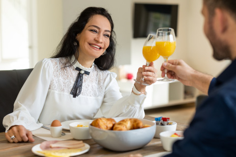 Couple enjoys breakfast with orange juice in Wellness Lodge XL at Hof van Salland, Netherlands, smiling.