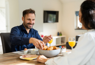 Man and woman enjoying breakfast with croissants and juice at Wellness Lodge XL, Hof van Salland, Netherlands.