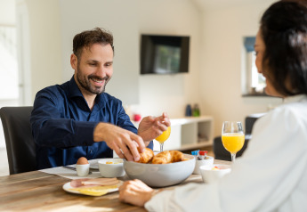Hombre y mujer desayunando croissants y jugo en Wellness Lodge XL, Hof van Salland, Países Bajos.