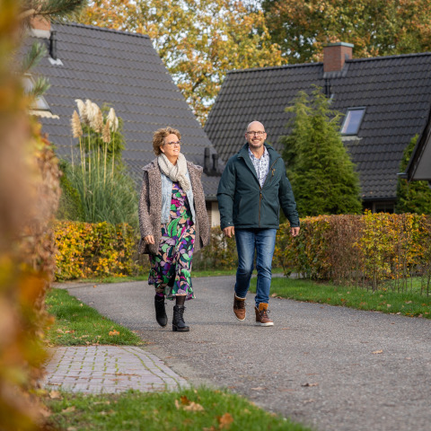 Two people walk on a path by Wellness Lodge XL at Hof van Salland, Netherlands, with lodges in the background.