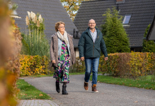 Two people walk on a path by Wellness Lodge XL at Hof van Salland, Netherlands, with lodges in the background.