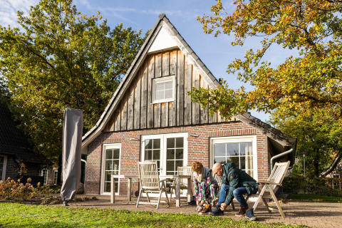 Una pareja frente a la casa pequeña Wellness Lodge XL en Hof van Salland, Países Bajos, en un día soleado.