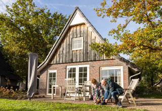 Una pareja frente a la casa pequeña Wellness Lodge XL en Hof van Salland, Países Bajos, en un día soleado.