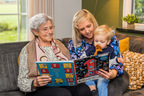 Tres generaciones leen juntas en una acogedora sala de Wellness Lodge XL en Hof van Salland, Países Bajos.