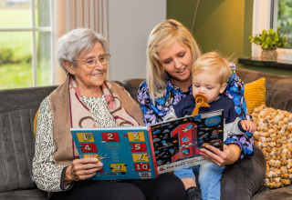 Three generations reading together in a cozy living room at Wellness Lodge XL at Hof van Salland, Netherlands.