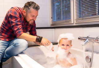 Padre jugando con su hijo en una bañera con burbujas en Wellness Lodge XL, Hof van Salland, Países Bajos.