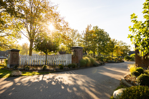 Entrada a Wellness Lodge XL en Hof van Salland, Países Bajos, con sol, árboles y jardines verdes.