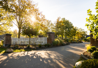Entrada a Wellness Lodge XL en Hof van Salland, Países Bajos, con sol, árboles y jardines verdes.