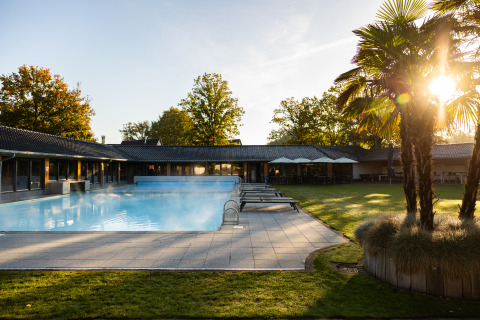 Piscina exterior en Wellness Lodge XL, Hof van Salland, Países Bajos, con tumbonas y palmeras al amanecer.