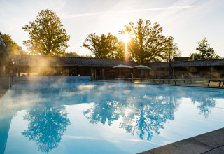 Piscina exterior humeante al sol de la mañana en Wellness Lodge XL en Hof van Salland, Países Bajos.