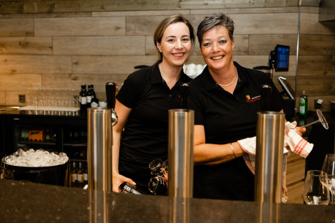 Two smiling women stand behind the bar at Wellness Lodge XL at Hof van Salland in the Netherlands.