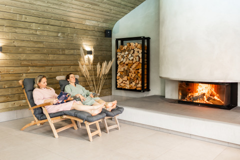 Dos personas descansan en sillones junto a la chimenea en Wellness Lodge XL, Hof van Salland, Países Bajos.