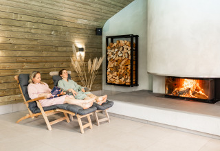 Two people relaxing on lounge chairs by the fireplace in the Wellness Lodge XL at Hof van Salland, Netherlands.