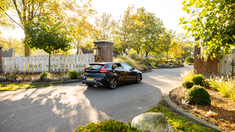 Coche negro en la entrada de Wellness Lodge XL en Hof van Salland, rodeado de árboles y jardines en Holanda.