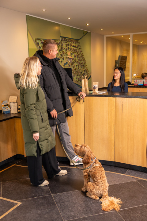 Pareja con perro realizando el check-in en la recepción de Wellness Lodge XL, Hof van Salland, Países Bajos.