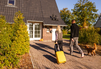 Un couple arrive avec une valise et un chien à la Wellness Lodge XL au Hof van Salland, aux Pays-Bas.